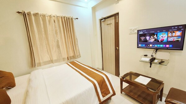 A hotel room with a bed, a TV mounted on the wall, a desk with a chair, and a door.