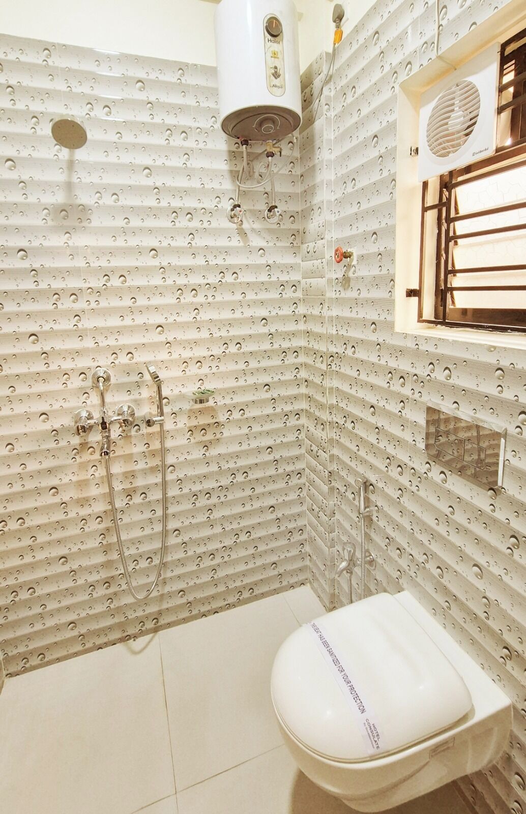 Un baño con inodoro blanco, ducha con cabezal de ducha de mano y calentador de pared.