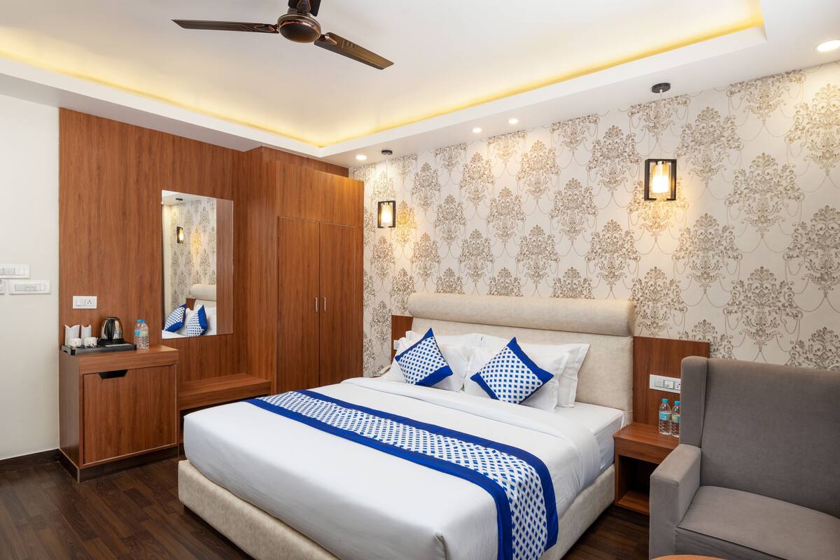 A hotel room with a bed, a desk, a chair, a ceiling fan, and a wall with patterned wallpaper.