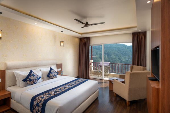 Une chambre d’hôtel avec un grand lit, une télévision, un balcon offrant une vue sur les montagnes et un ventilateur de plafond.
