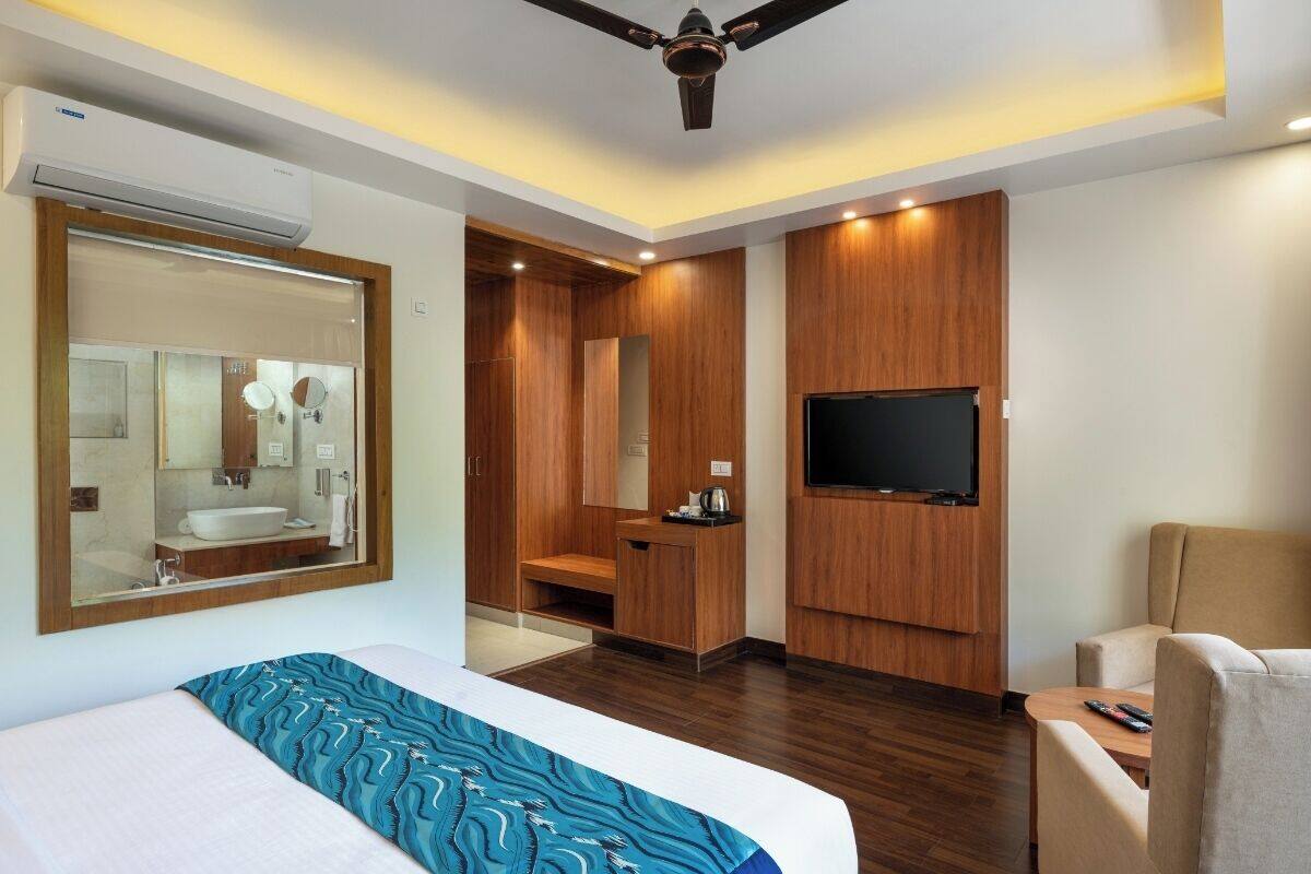 A hotel room with a bed, a TV, a seating area, and a bathroom with a mirror and sink.