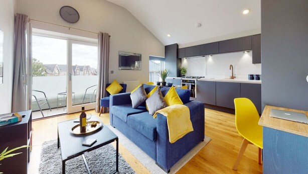 A modern living room with a sofa, a dining table, and a kitchen area.