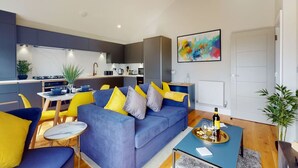 A modern living room with a blue sofa, yellow cushions, and a dining area with a small table and chairs.