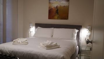 Una habitación de hotel con una cama grande, ropa de cama blanca, dos lámparas de noche y un cuadro en la pared.