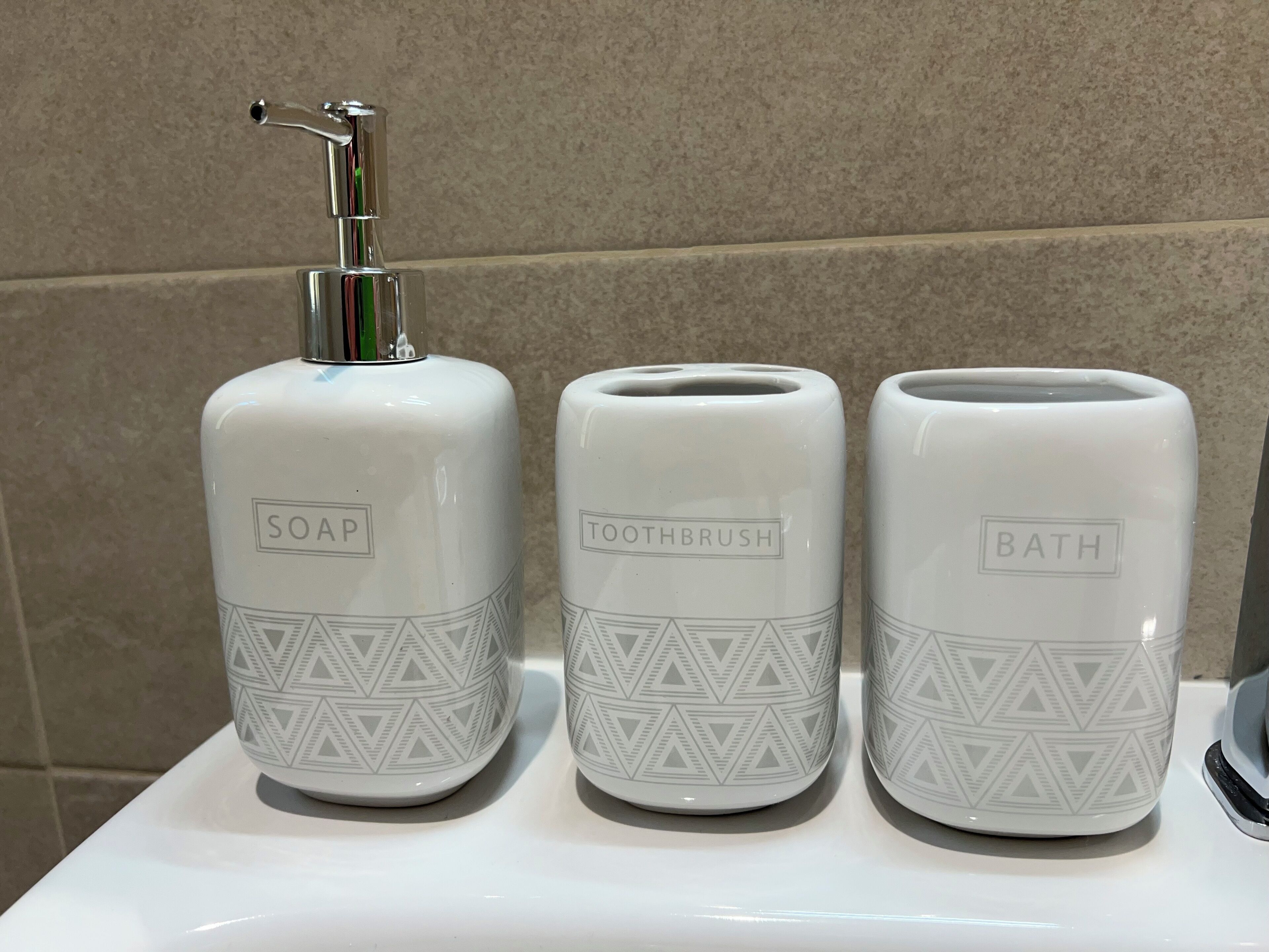 Trois distributeurs de produits d’hygiène, étiquetés « savon », « brosse à dents » et « produits de bain », sont posés sur un comptoir blanc.