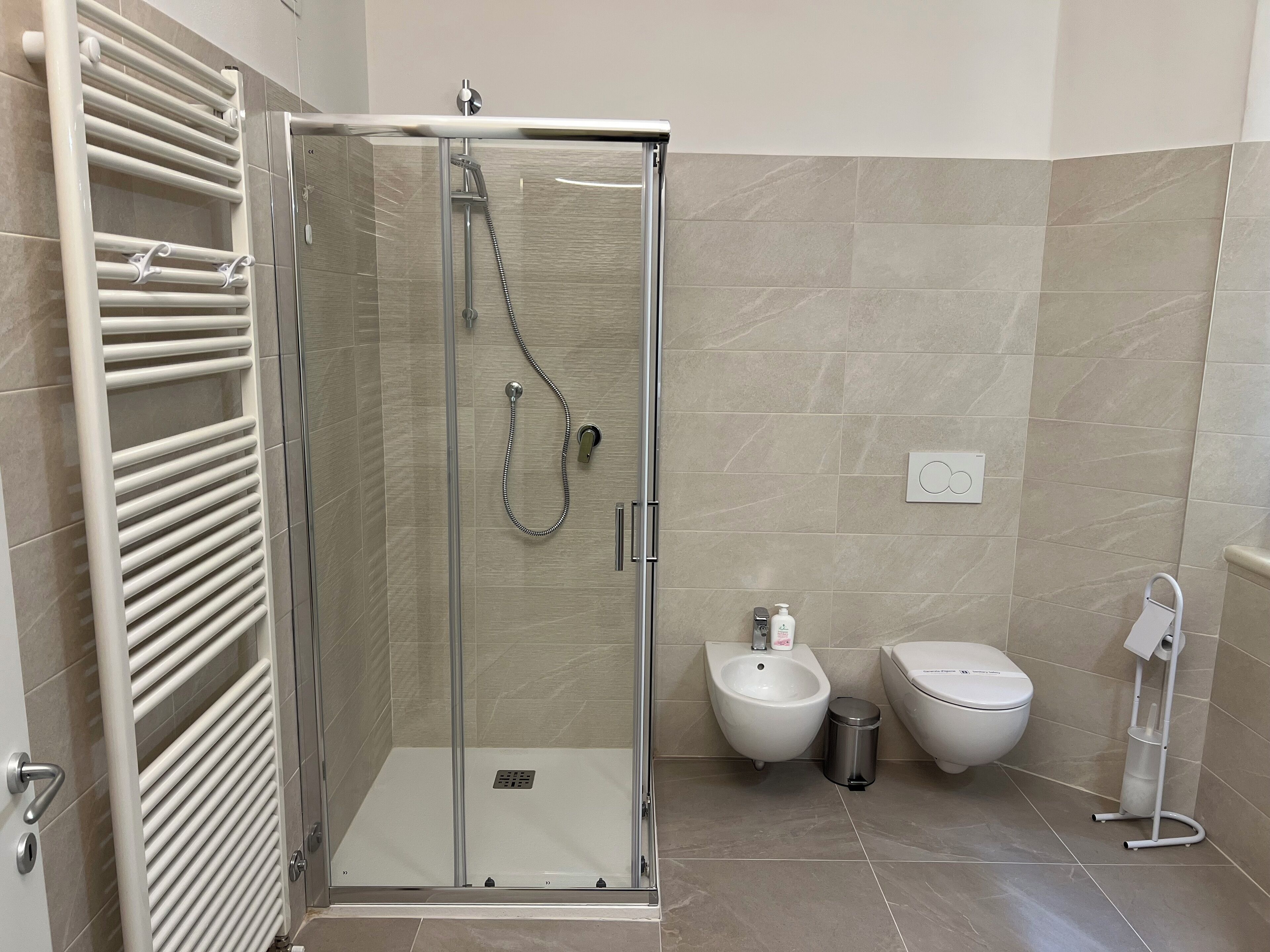 Un baño moderno con ducha de vidrio, inodoro blanco, bidé y toallero.