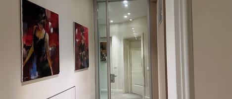 A hallway with two paintings on the wall, a glass door leading to another room, and a carpeted floor.