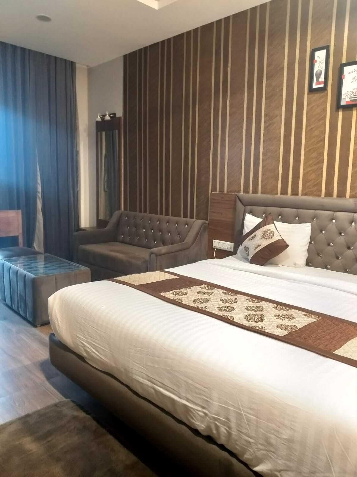 A bedroom with a large bed, a tufted headboard, a side table, and a wall with vertical stripes.