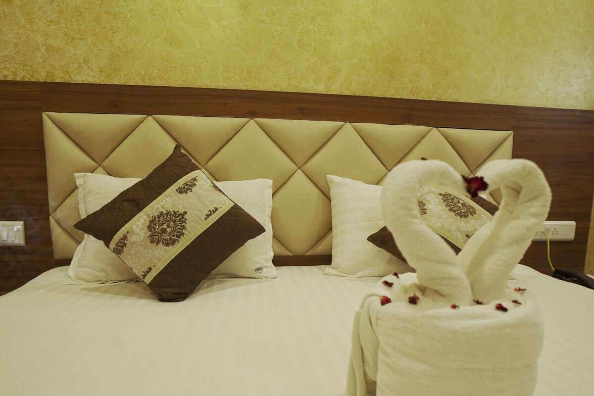 A hotel room with a bed, two pillows, and a towel shaped like swans.