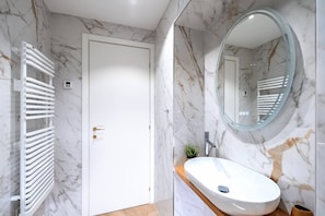 A modern bathroom with marble walls, a white door, a round mirror, and a white sink.