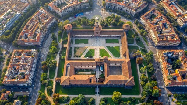 Luchtbeeld van een historisch ommuurd stadscentrum met een centraal plein, omgeven door gebouwen en groen.