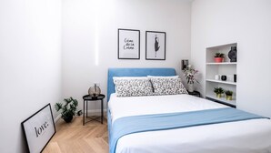 Een slaapkamer met een bed, een nachtkastje, een plank met planten en twee ingelijste foto’s aan de muur.