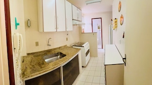 A compact kitchen with white cabinets, a granite countertop, a sink, a stove, and a refrigerator. - Tropical Beach / Center - Cabo Frio (Cabo Frio)