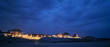 A coastal town at dusk with illuminated buildings and a calm sea.