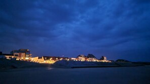 A coastal town at dusk with illuminated buildings and a calm sea.