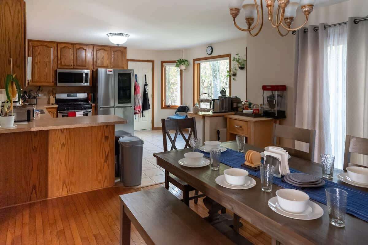A kitchen with wooden cabinets, a microwave, a stove, and a refrigerator. There is a dining table set with plates, glasses, and a bench.