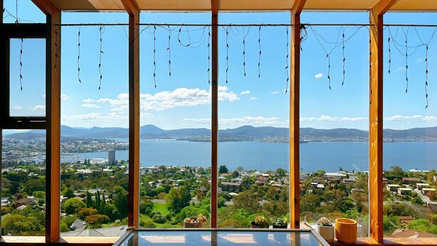 Una stanza con ampie finestre vista su un lago e sullo skyline cittadino, travi in legno e un tavolo in vetro.