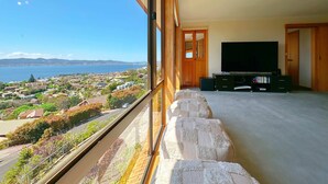 Un soggiorno moderno con una grande TV, gradini in pietra che conducono a un balcone e vista su una cittadina costiera.