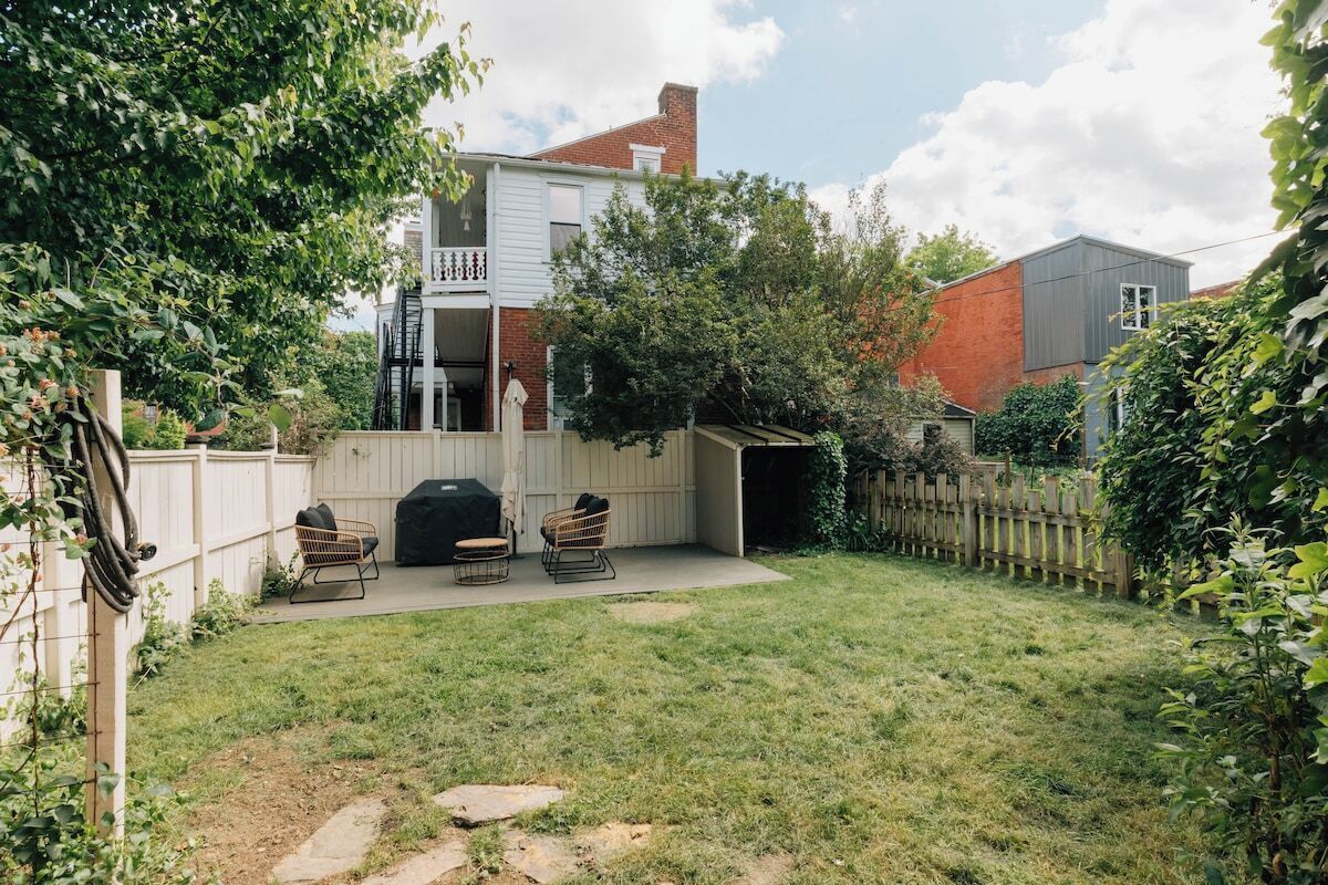 Un giardino con un'area barbecue, due poltrone in vimini, una recinzione in legno e una casa con un balcone.