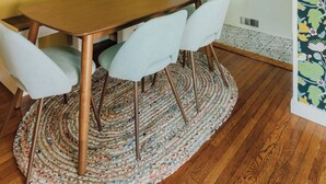 A dining area with a wooden table and four chairs, a colorful abstract painting on the wall, and a kitchen visible through an open doorway. - The Garden House (Lancaster)