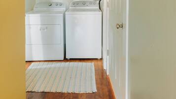 A laundry room with two white front-loading washers and dryers, a striped rug on the wooden floor, and a door leading to another room.