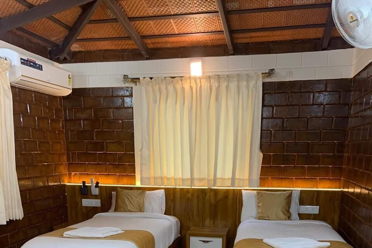 A room with two beds, a wooden bench, a ceiling fan, and a brick wall.