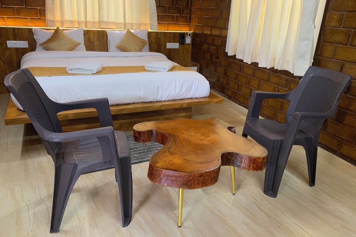 A hotel room with a bed, two chairs, a wooden coffee table, and a brick wall.