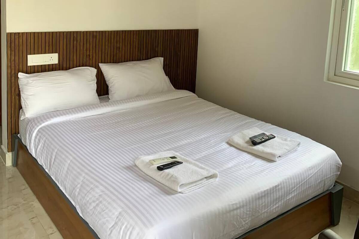 A neatly made bed with white linens and pillows, a wooden headboard, and a window with a view.