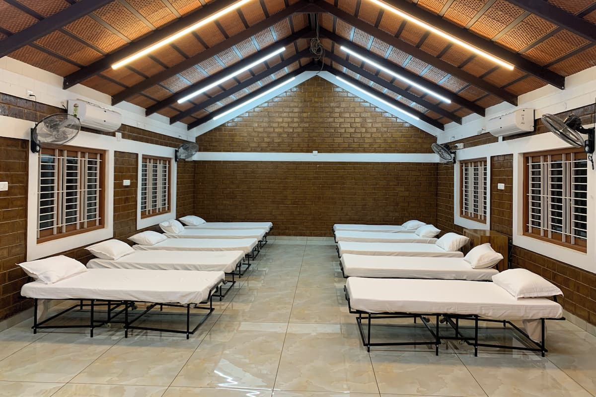 A room with multiple beds arranged in rows, a sloped ceiling with exposed beams, and brick walls.