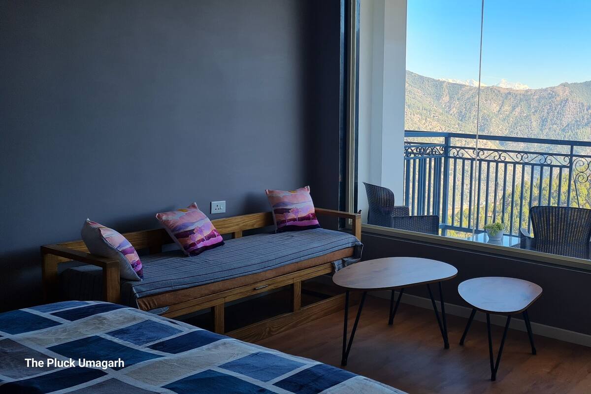 Un balcón con vistas a montañas, un banco de madera con cojines y dos mesitas.