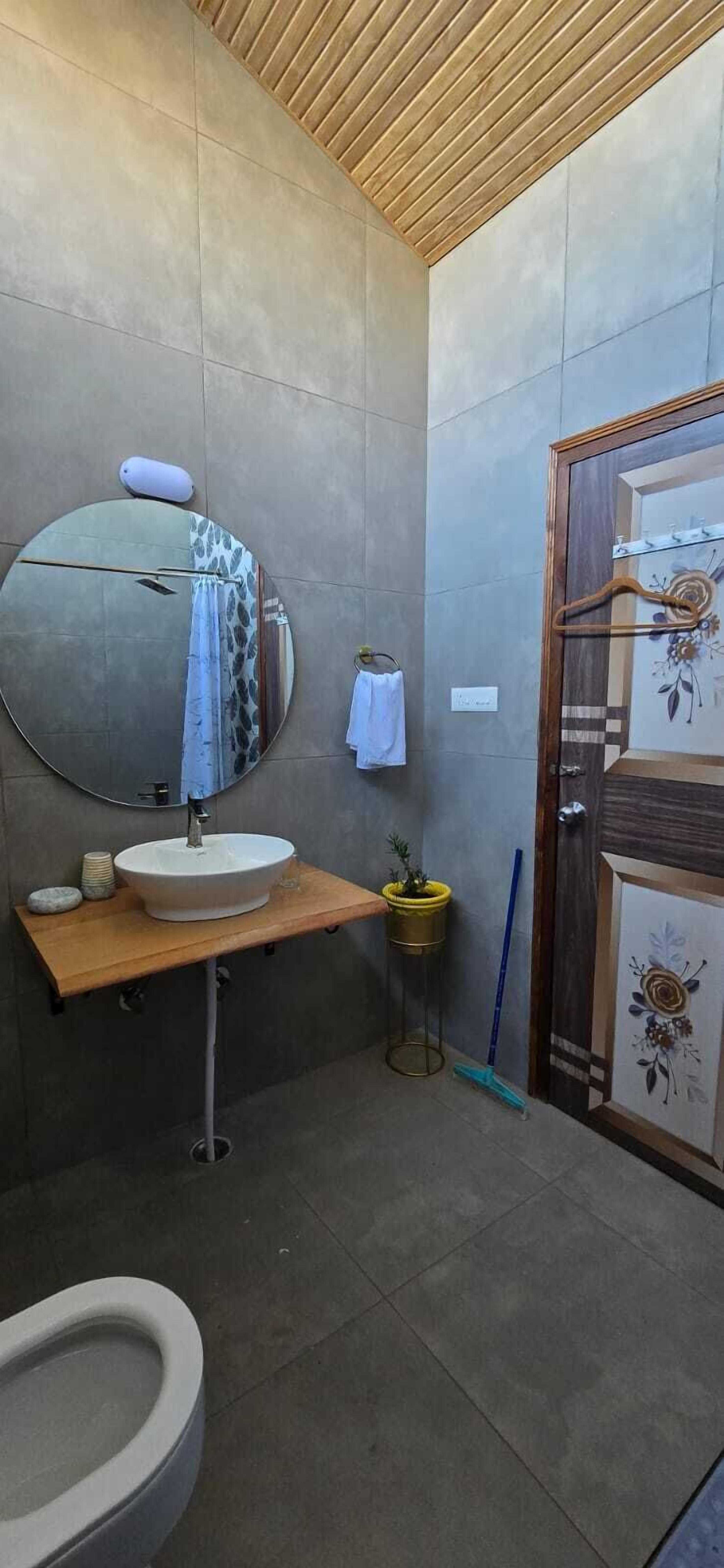A bathroom with a round mirror, a sink, a toilet, and a shower area.