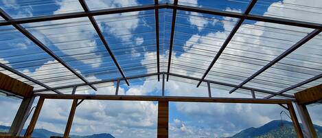 A room with a glass ceiling, wooden beams, and a view of mountains.
