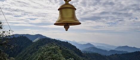 A large golden bell suspended in the air with a mountainous landscape in the background.