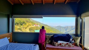 Une pièce avec un lit, une fenêtre donnant sur une montagne et une personne debout près de la fenêtre.