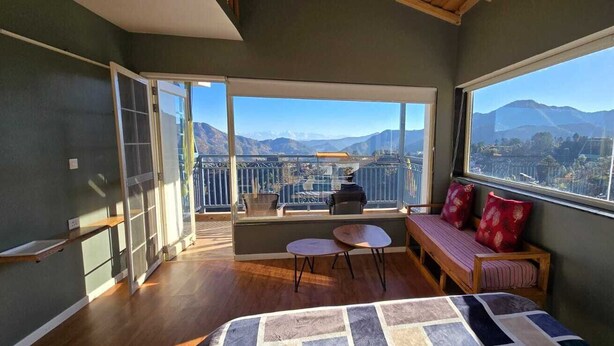 Un balcon avec vue sur les montagnes, un banc en bois, une petite table et un lit recouvert d’une courtepointe à motifs.