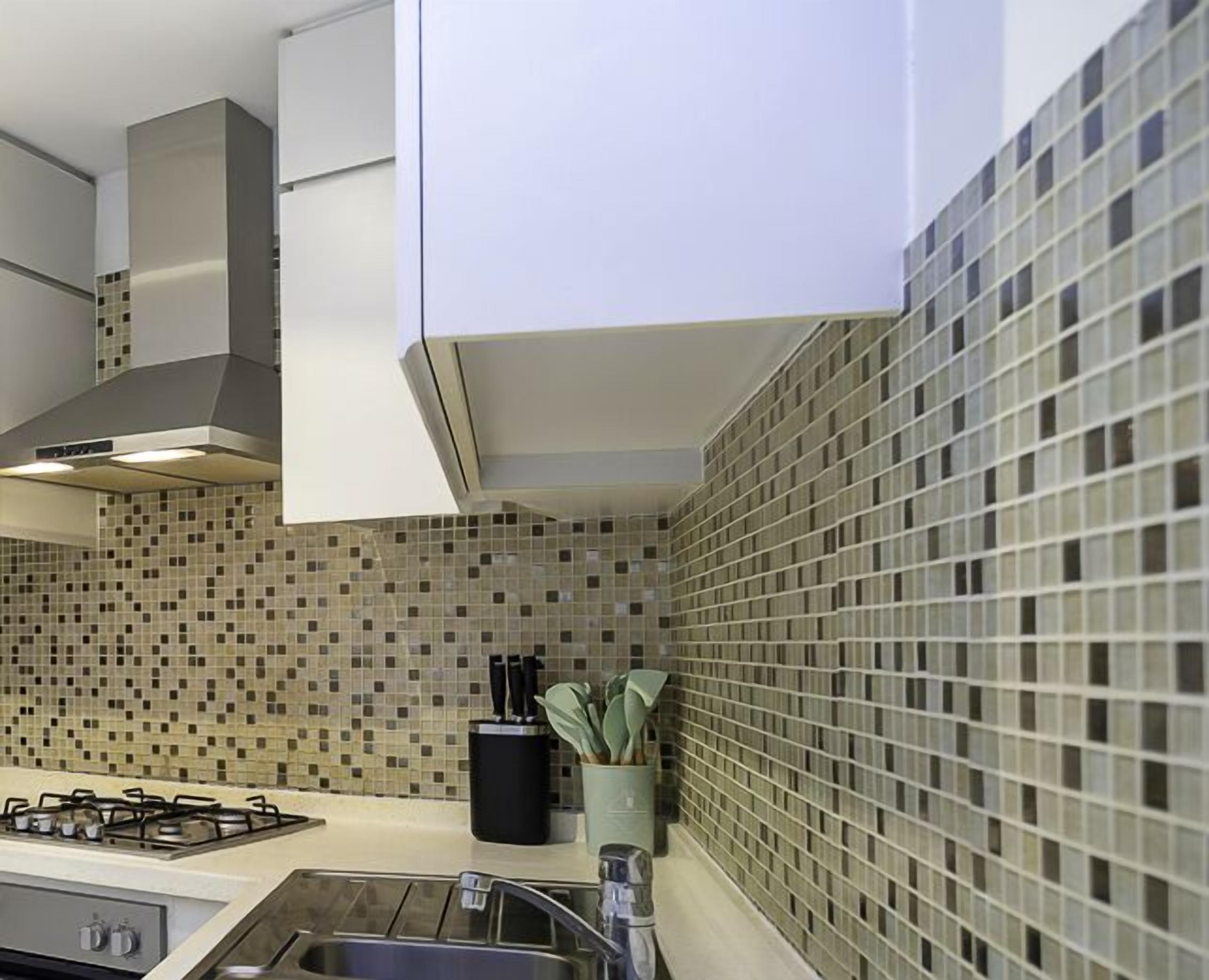 Une cuisine équipée d’une cuisinière à gaz, d’un évier et d’un crédence décorée de mosaïques.