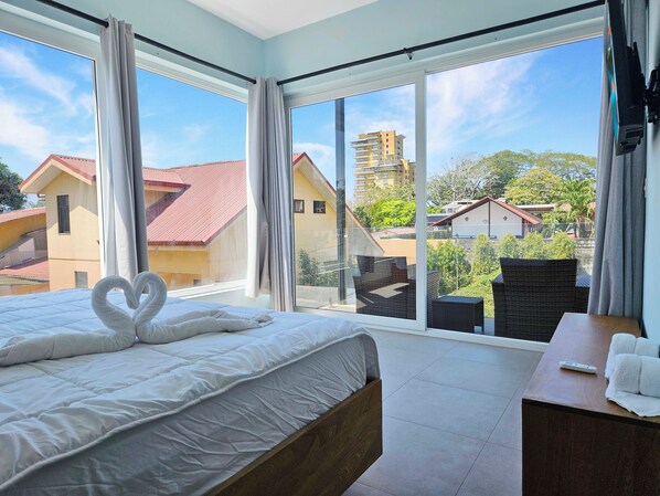 Une chambre d’hôtel avec un grand lit, une table de chevet, une télévision et une vue sur des immeubles et des arbres.