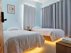 A bedroom with two beds, a bedside table with a picture frame, a wooden nightstand, and a small table with towels.