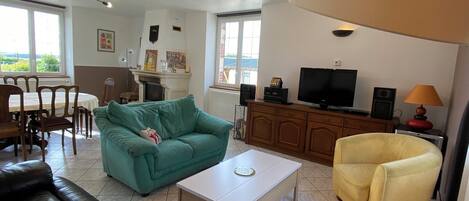 A living room with a green sofa, a black leather couch, a yellow armchair, a white coffee table, and a TV on a wooden cabinet.