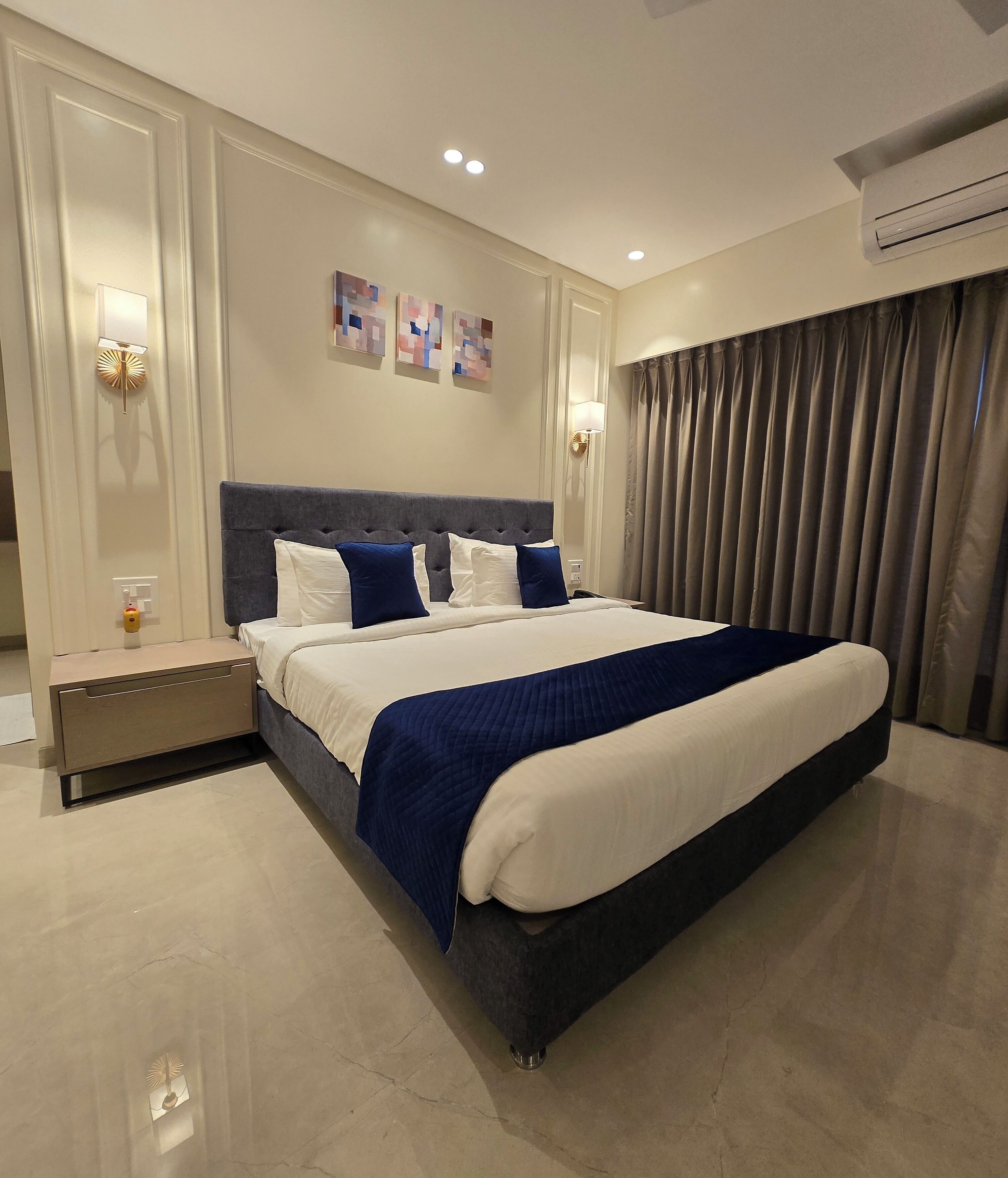 Une chambre d’hôtel moderne avec un grand lit, une table de chevet, un climatiseur fixé au mur et une fenêtre avec des rideaux.