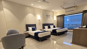 A hotel room with two beds, a desk, a chair, and a large window with a view. - Western Hotel (Chandrapur)