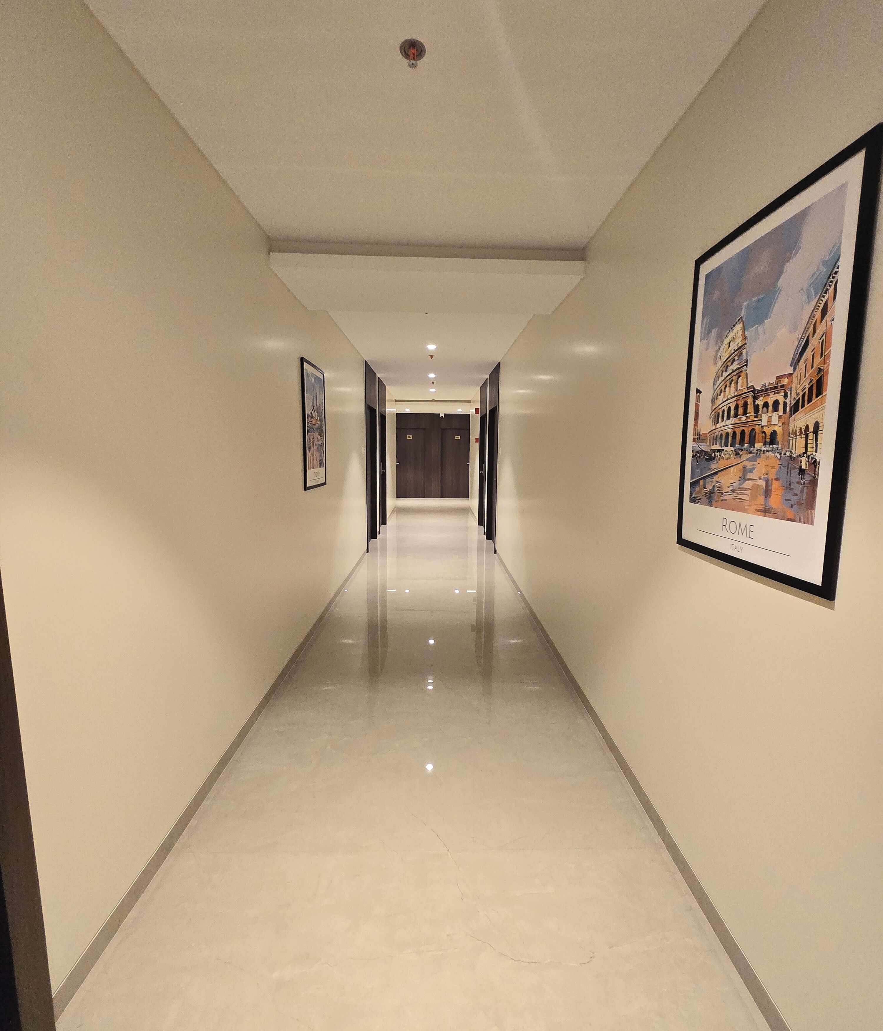 A hotel corridor with a polished floor, framed artwork on the walls, and a framed picture of Rome.