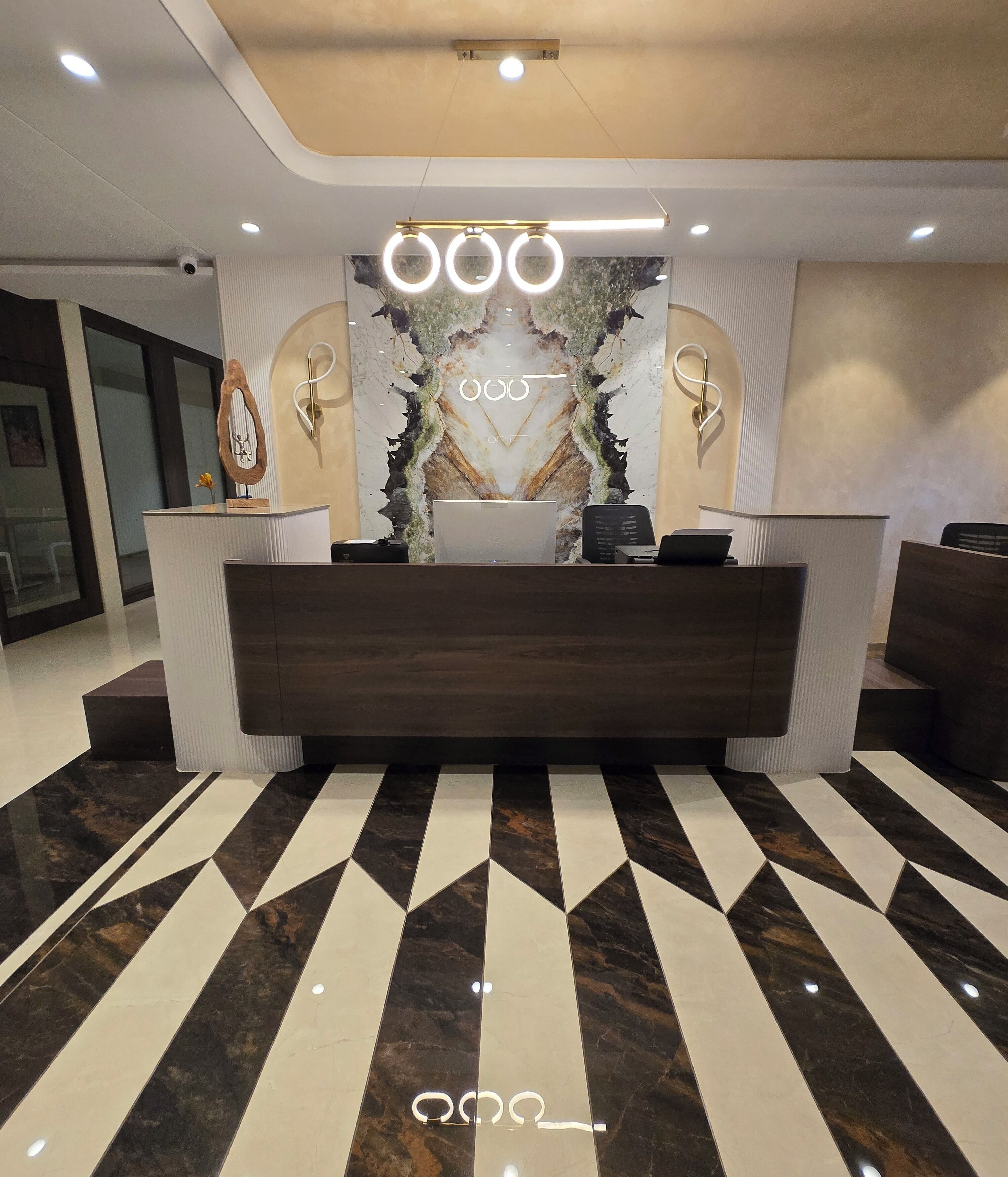 Un espace d’accueil au design moderne, avec un sol à motifs de marbre, un comptoir d’accueil central et un mur décoratif orné d’un motif original.