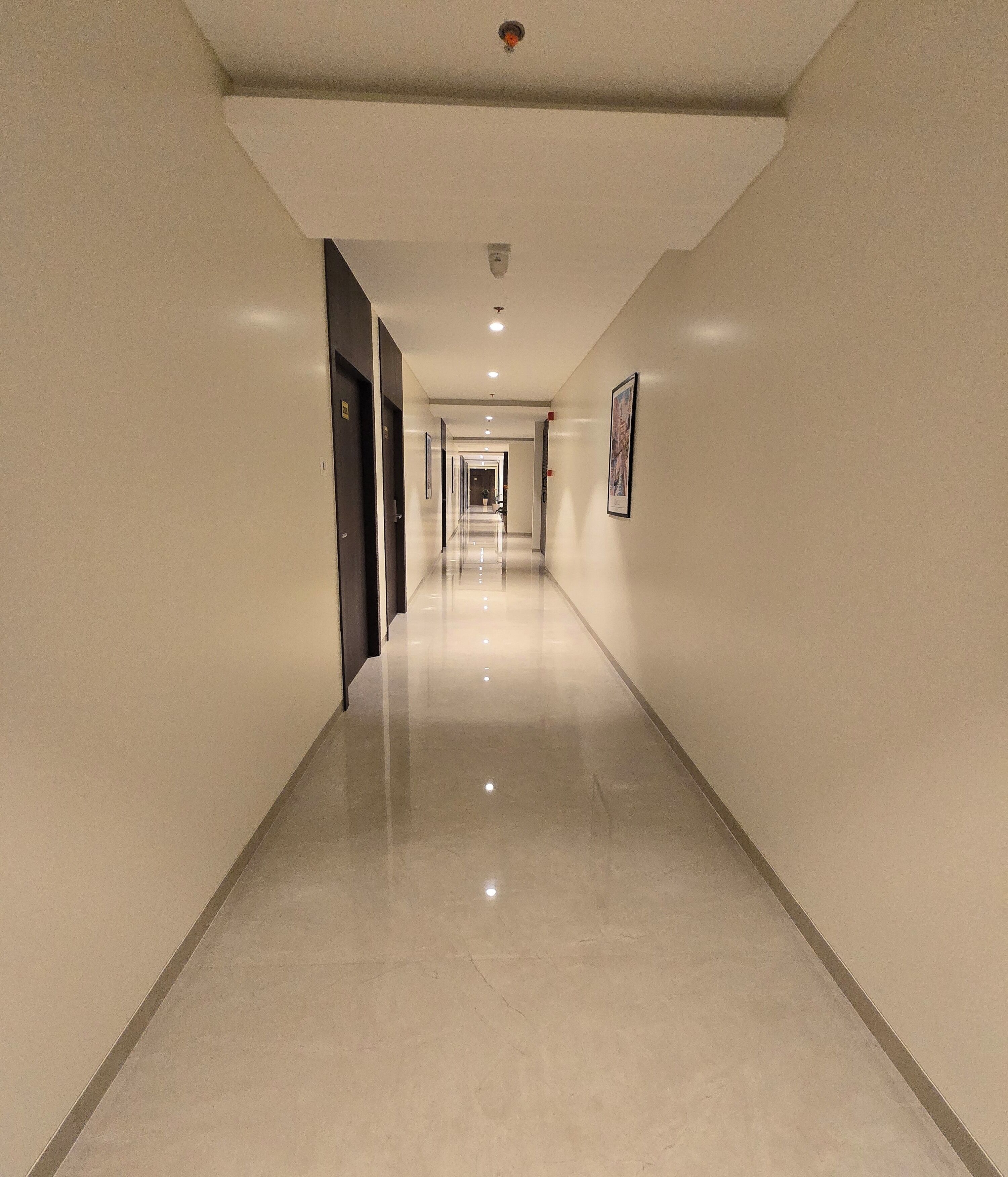 A long, narrow hallway with a shiny floor, doors on both sides, and a ceiling light.