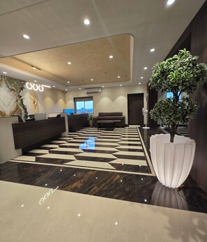 A modern lobby with a geometric patterned floor, a reception desk, a sofa, and a large potted plant. - Western Hotel (Chandrapur)