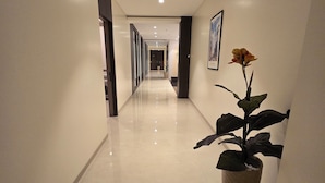 A long, well-lit hallway with a large potted plant and framed pictures on the walls. - Western Hotel (Chandrapur)