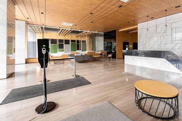 A modern lobby with a wooden ceiling, a reception desk, seating area, and a marble wall.