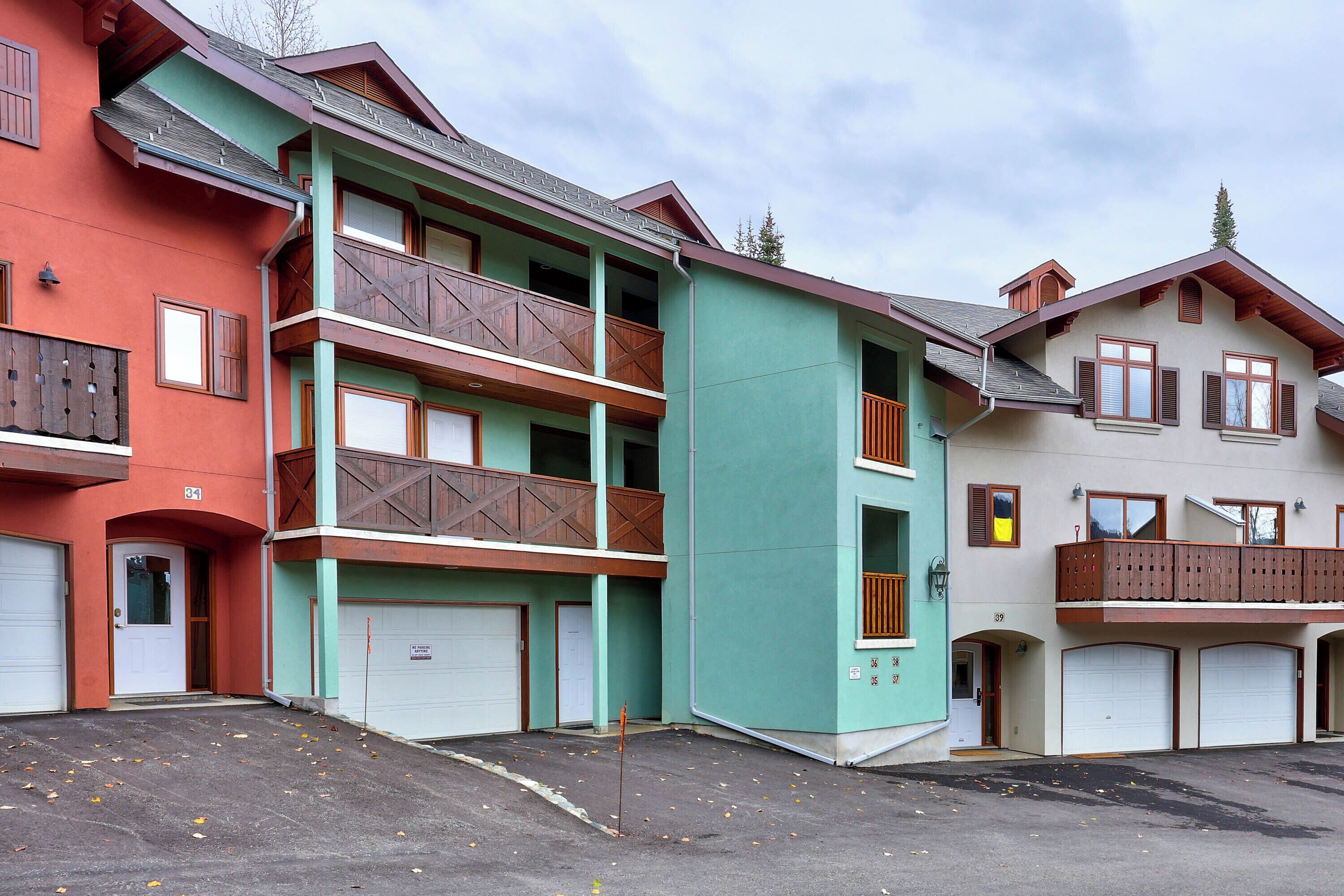 Un edificio residencial de varios pisos con balcones, puertas de garaje y una zona de estacionamiento.