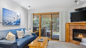 A modern living room with a blue sofa, a wooden coffee table, a flat-screen TV, and a fireplace. - Upper floor 2 bedroom condo, great location close to village centre and next to ski runs (Sun Peaks)