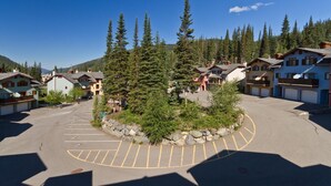 A parking lot with a central landscaped area surrounded by buildings with a mountainous backdrop. - Upper floor 2 bedroom condo, great location close to village centre and next to ski runs (Sun Peaks)